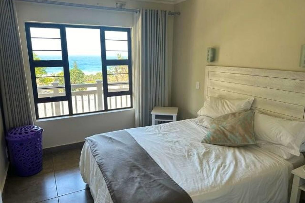 A bright bedroom featuring tiled floors, a ceiling fan, and a large window offering scenic ocean views.