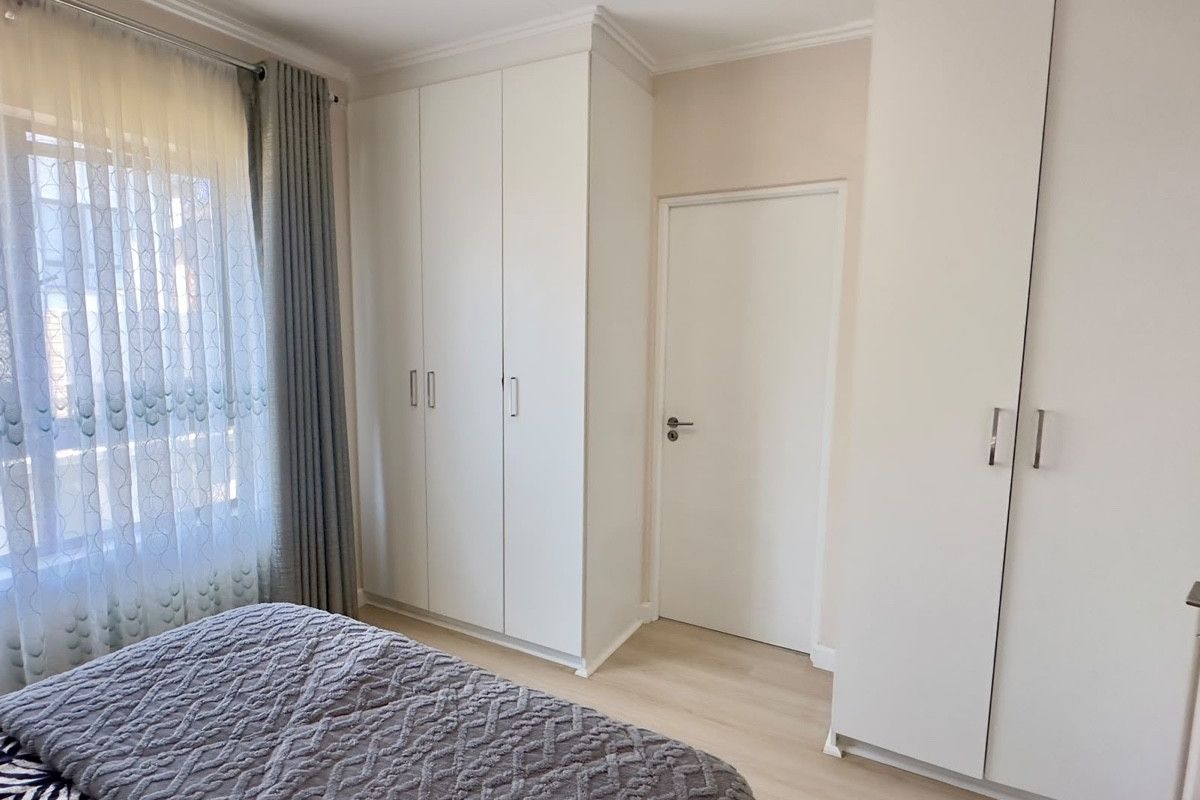 A well-maintained bedroom featuring light-toned laminate flooring, ample built-in cupboard storage, and neutral wall finishes.