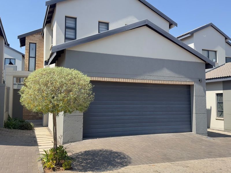 Front elevation of a modern double-storey house featuring a double garage, paved driveway, and contemporary grey and white exterior finishes.