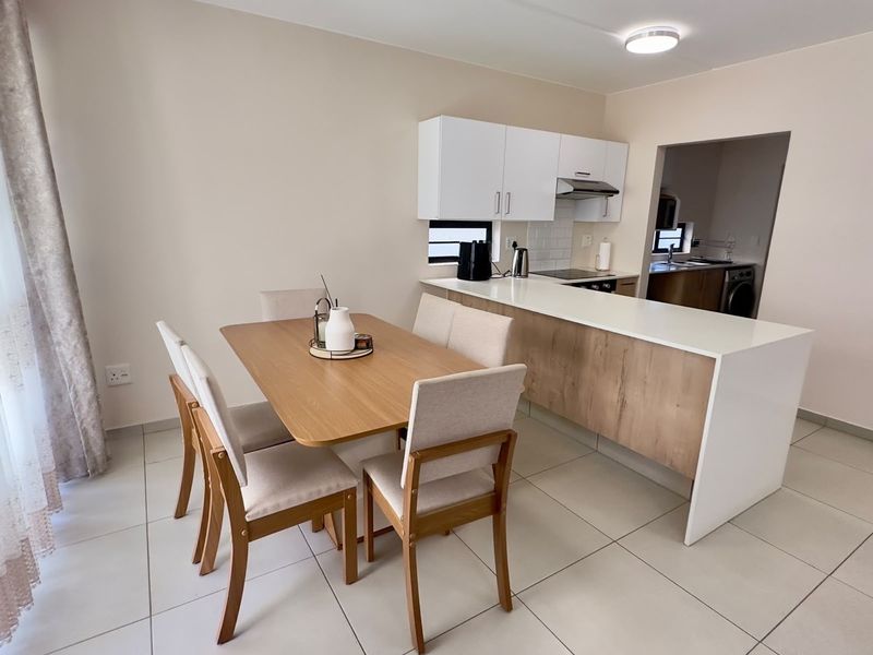 Modern open-plan kitchen and dining area featuring sleek cabinetry, a functional island, and neutral tiled flooring throughout.