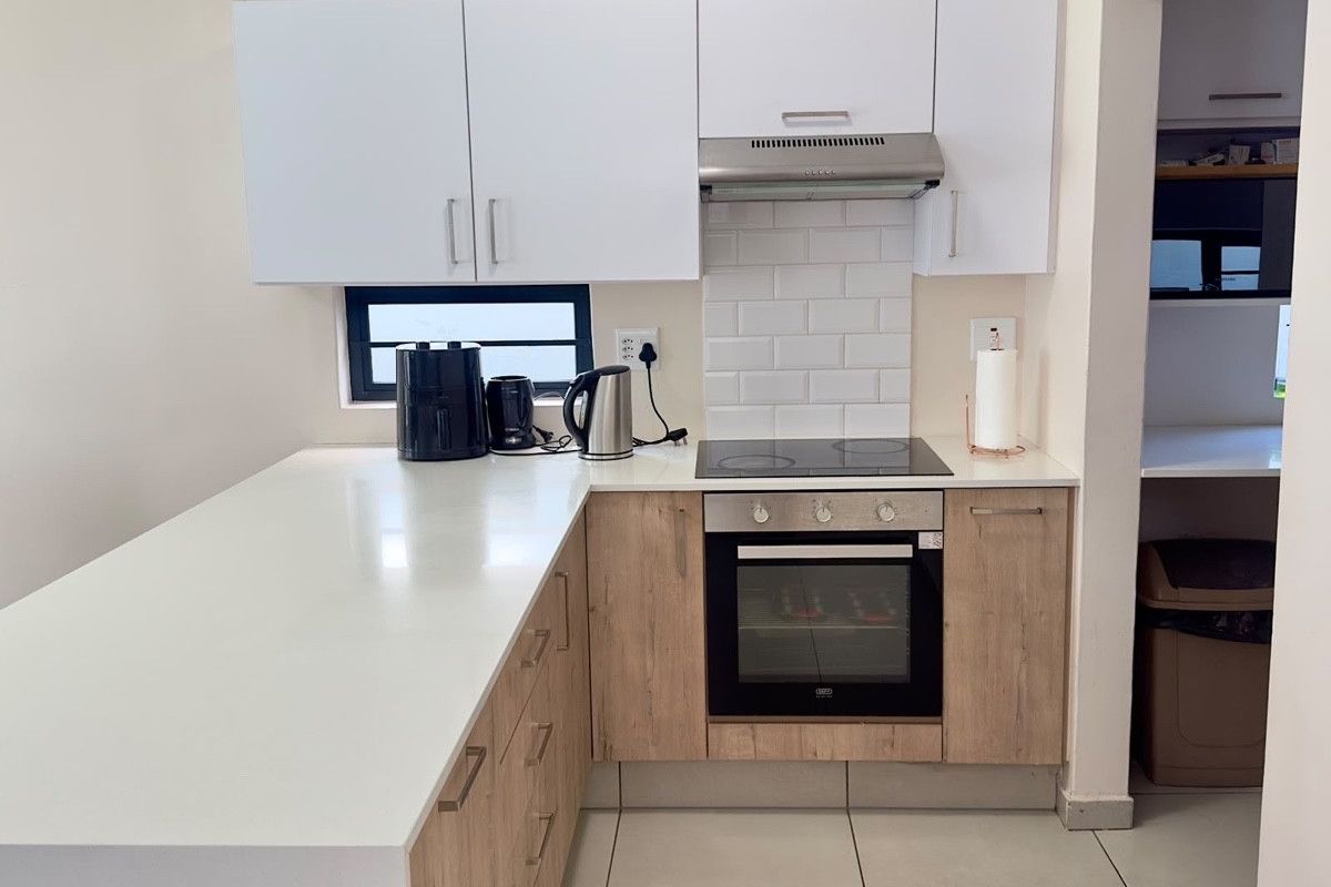 Modern kitchen featuring light wood-finish cabinetry, white quartz countertops, a subway tile backsplash, and integrated stainless steel appliances.