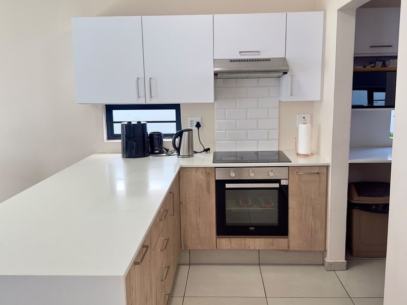 Modern kitchen featuring light wood-finish cabinetry, white quartz countertops, a subway tile backsplash, and integrated stainless steel appliances.