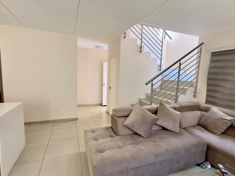 A bright and modern living area featuring neutral tiled flooring and a contemporary staircase with a stainless steel balustrade.