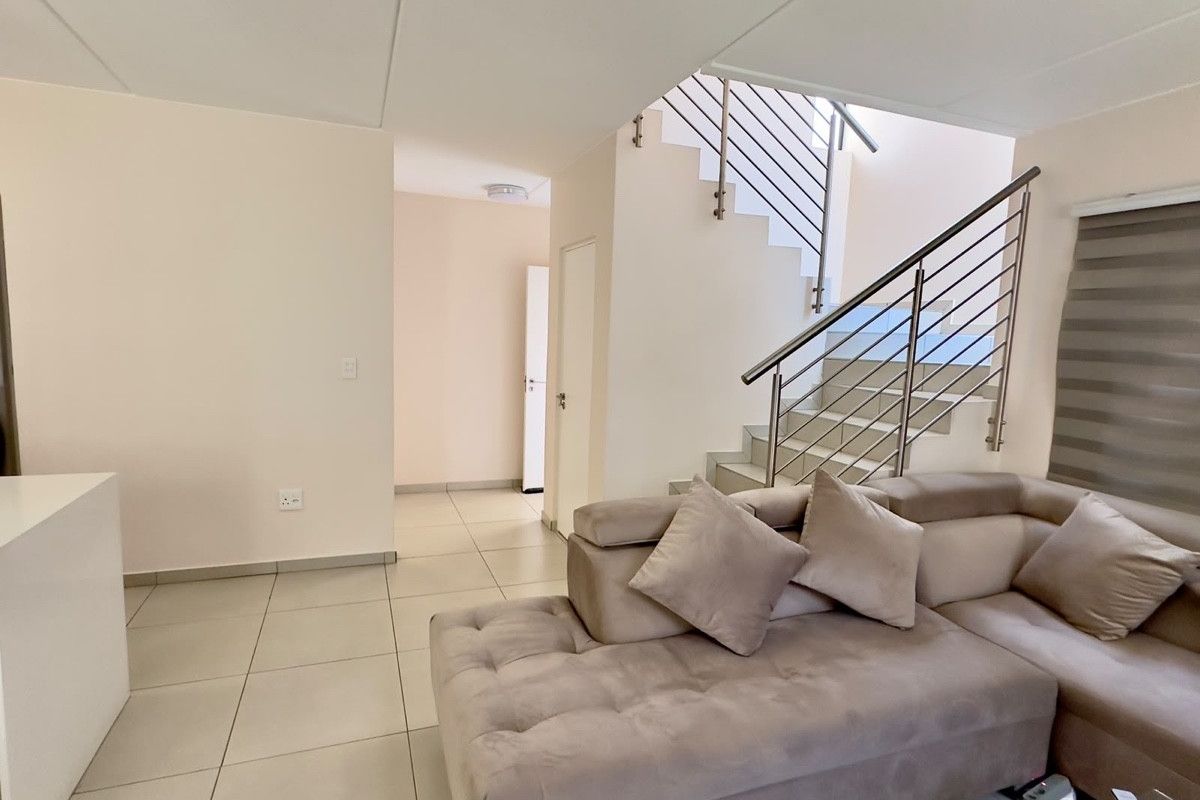 A bright and modern living area featuring neutral tiled flooring and a contemporary staircase with a stainless steel balustrade.