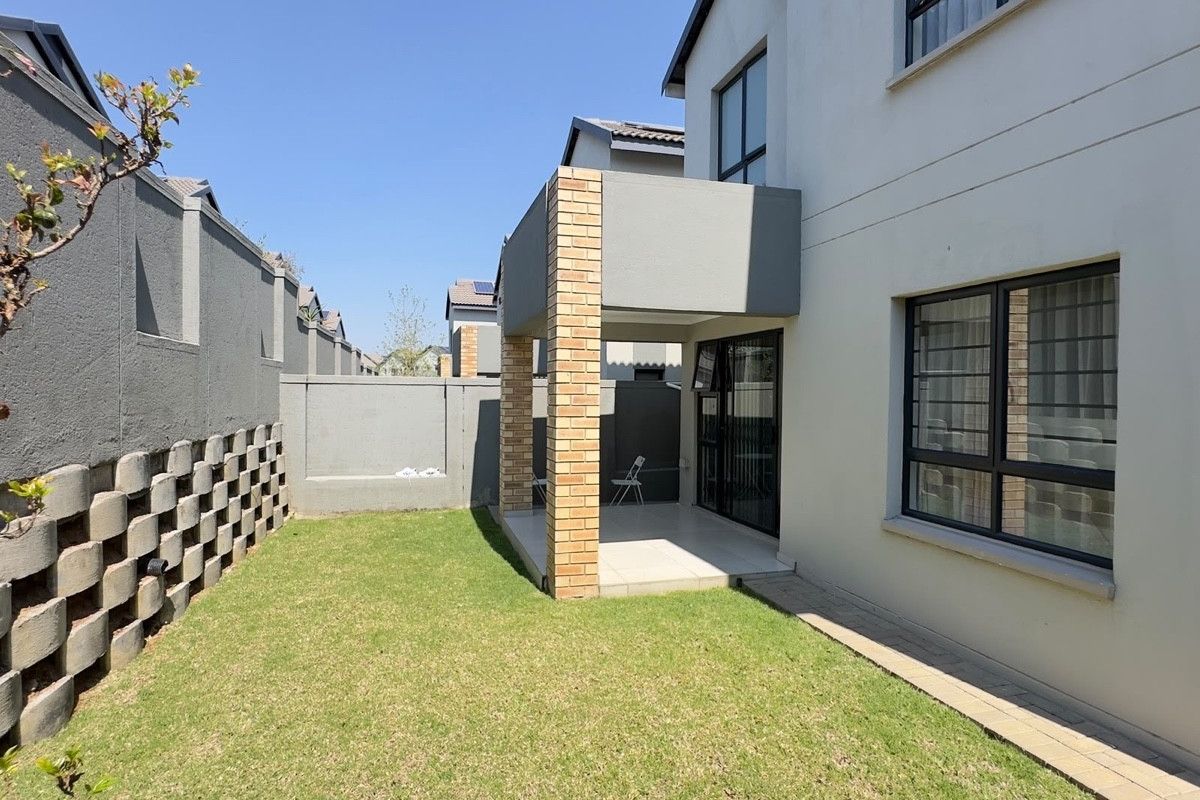 Rear view of the property featuring a covered patio, a small private lawn, and a secure boundary wall.
