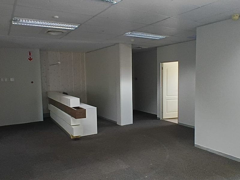 An empty office space featuring a built-in reception desk, suspended ceiling with fluorescent lighting, and carpeted flooring.