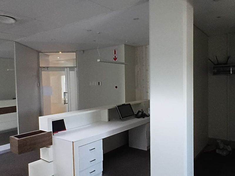 Office reception area featuring a built-in desk, glass partition door, and recessed ceiling lighting, providing a functional workspace entry point.