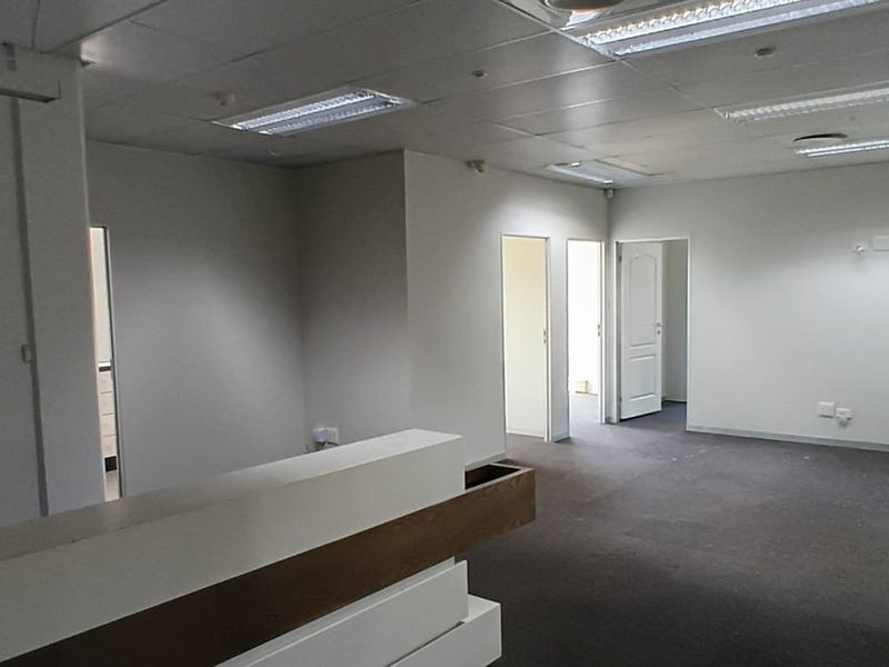 An empty office space featuring a built-in reception desk, suspended ceiling with recessed lighting, and carpeted flooring.