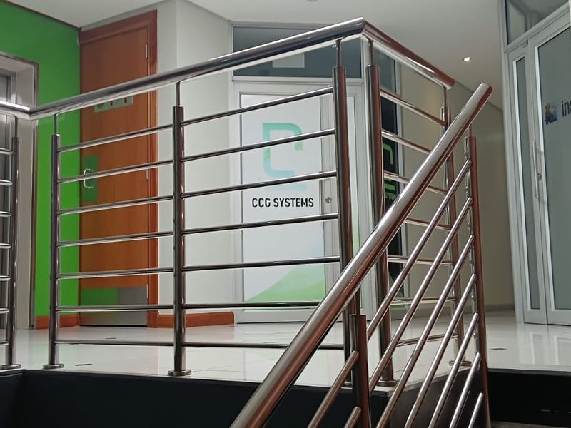 A modern office building hallway featuring a stainless steel balustrade, elevator access, and professional glass-paneled office doors.