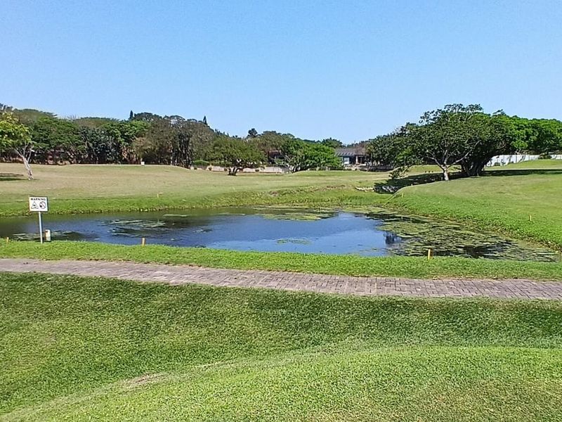 A well-maintained landscaped garden area featuring a central water feature, expansive green lawns, and a paved walkway.