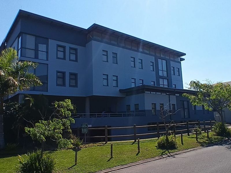A modern multi-story office building exterior featuring a contemporary facade, timber fencing, and well-maintained surrounding landscaping.