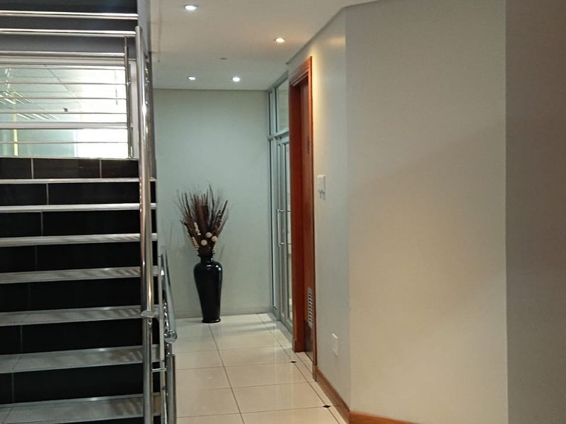 Modern office building hallway featuring a tiled staircase with stainless steel railings, recessed lighting, and access to an elevator.