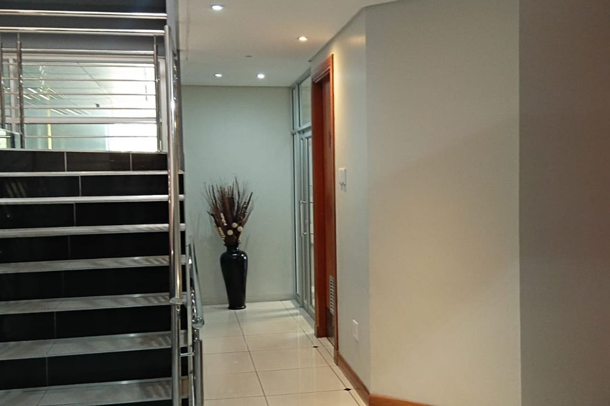Modern office building hallway featuring a tiled staircase with stainless steel railings, recessed lighting, and access to an elevator.