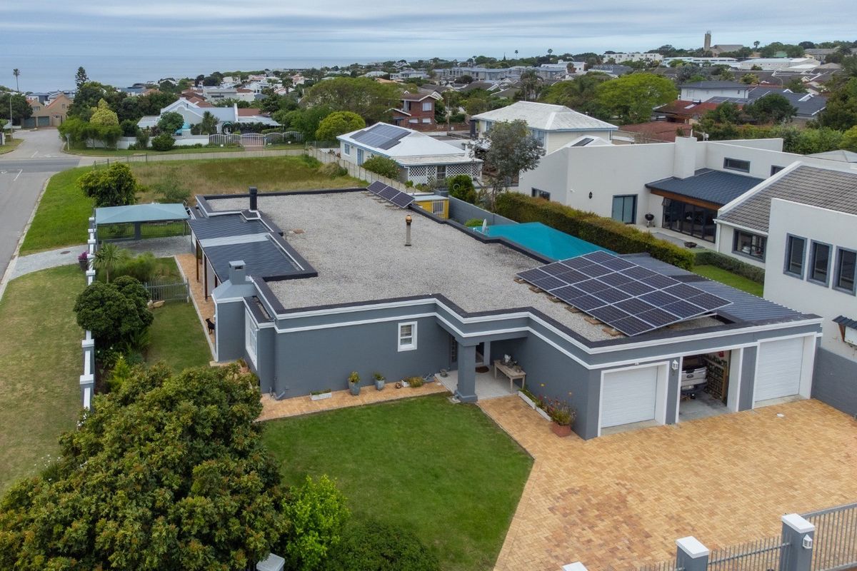 Aerial view of a modern single-story home featuring a flat roof with solar panels, a double garage, paved driveway, and a private swimming pool.