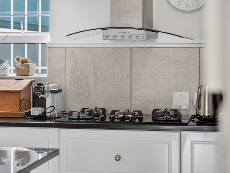 A well-maintained kitchen area featuring a modern gas hob, stainless steel extractor fan, stone tile splashback, and granite countertops with white cabinetry.