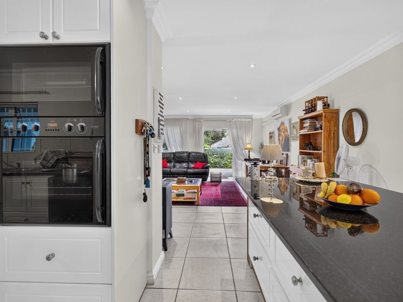 An open-plan living and kitchen area featuring a modern built-in oven, dark granite countertops, tiled floors, and direct access to the outdoor patio.