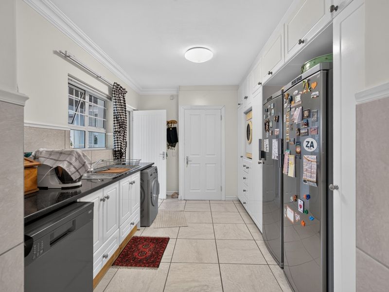A well-maintained laundry room featuring white built-in cabinetry, granite countertops, a stainless steel sink, and tiled flooring.