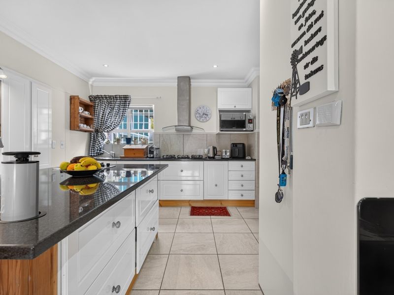 A well-maintained kitchen featuring white cabinetry, granite countertops, a central island, and modern built-in appliances with tiled flooring.