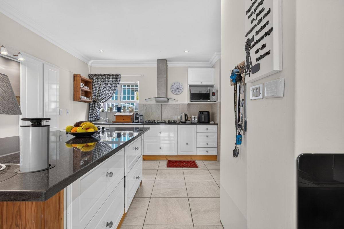 A well-maintained kitchen featuring white cabinetry, granite countertops, a central island, and modern built-in appliances with tiled flooring.