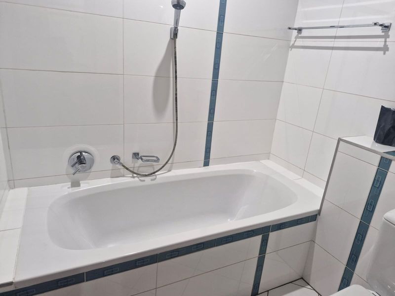 A clean, functional bathroom featuring a built-in bathtub with a handheld shower attachment and decorative tiled accents.