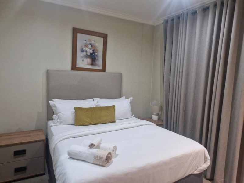 A well-maintained bedroom featuring neutral wall tones, crown molding, and full-length curtains.