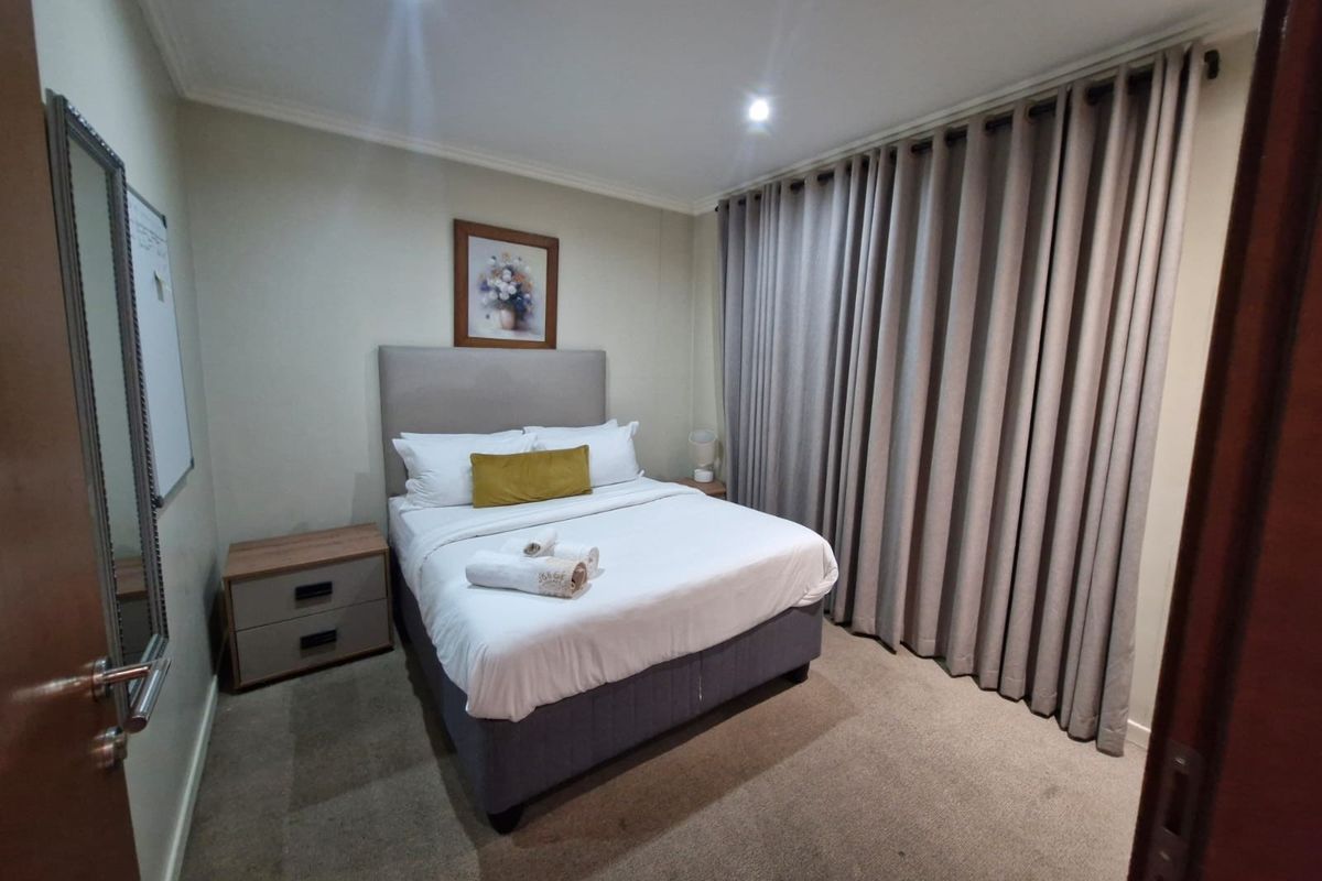 A well-maintained bedroom featuring recessed downlighting, neutral wall finishes, carpeted flooring, and full-length curtains providing privacy.