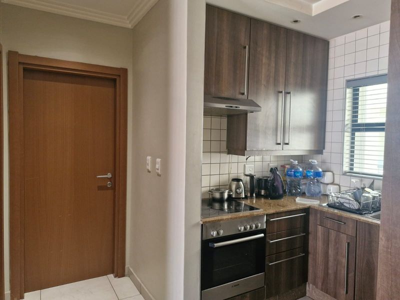 Compact kitchen featuring dark wood cabinetry, granite countertops, built-in oven and hob, and a tiled backsplash, adjacent to a wooden interior door.