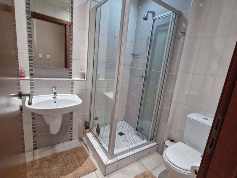 A clean and functional bathroom featuring a glass shower enclosure, wall-mounted basin, toilet, and neutral tiled finishes throughout.
