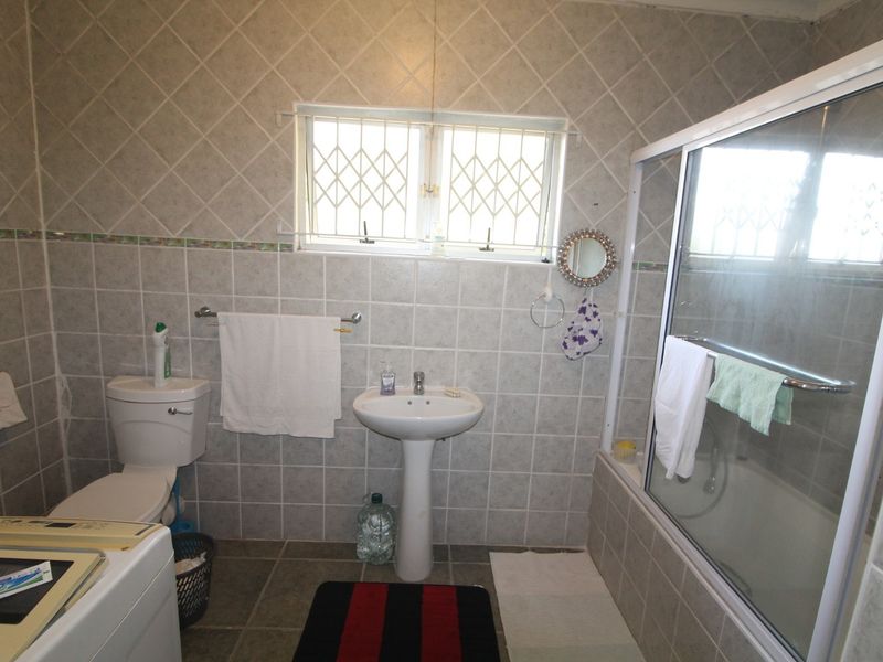 A functional bathroom featuring a pedestal basin, toilet, and a shower enclosure with tiled walls and flooring throughout.