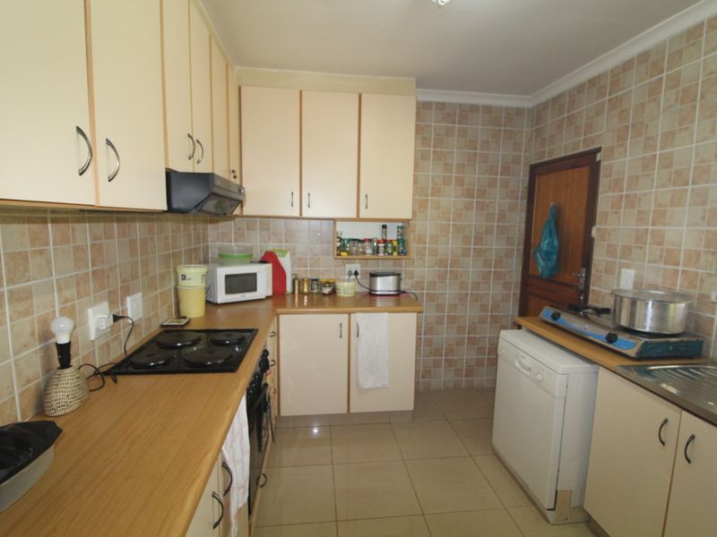 A functional kitchen featuring laminate countertops, built-in cabinetry, an electric hob with extractor fan, and tiled backsplash and flooring.