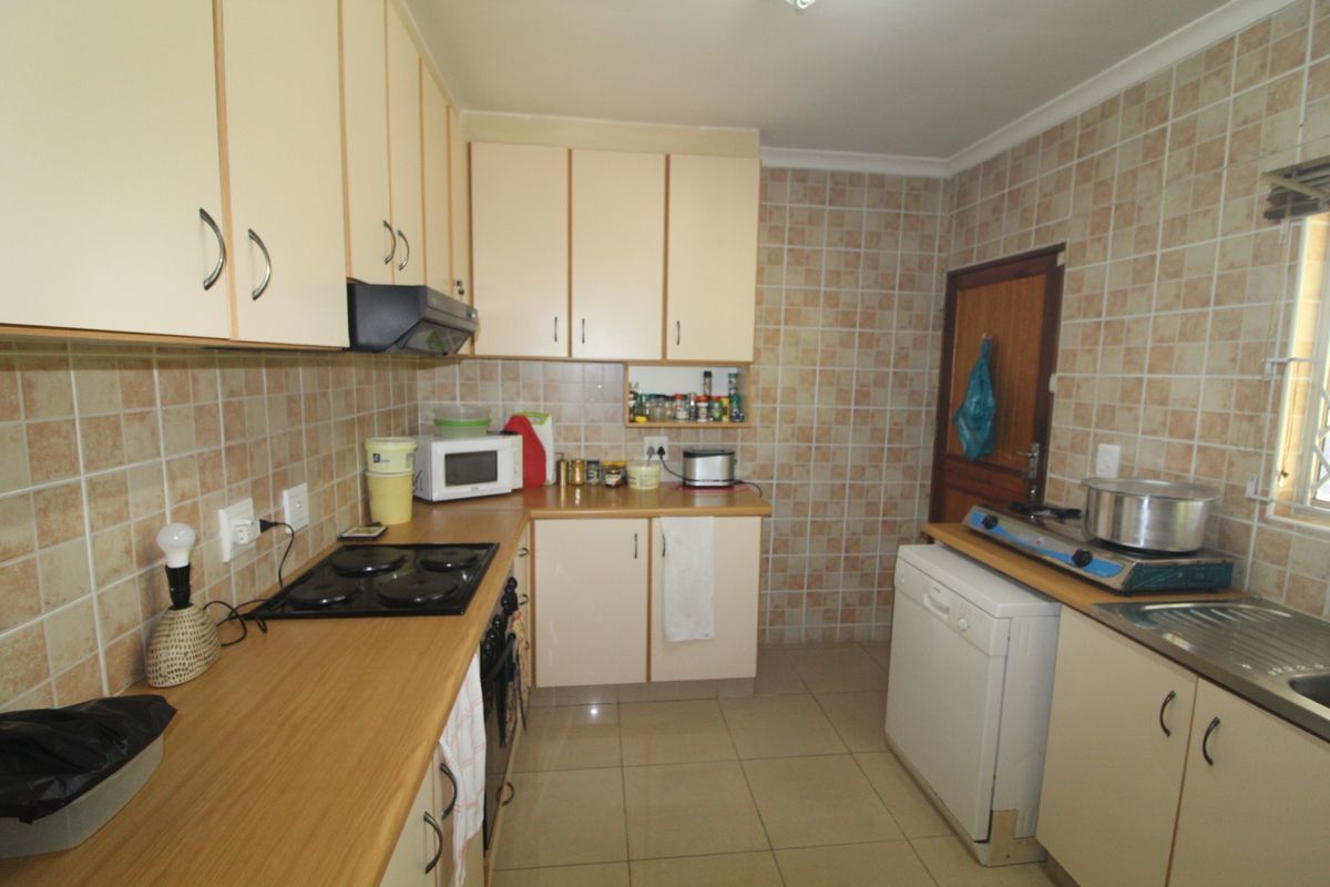A functional kitchen featuring laminate countertops, built-in cabinetry, an electric hob with extractor fan, and tiled backsplash and flooring.