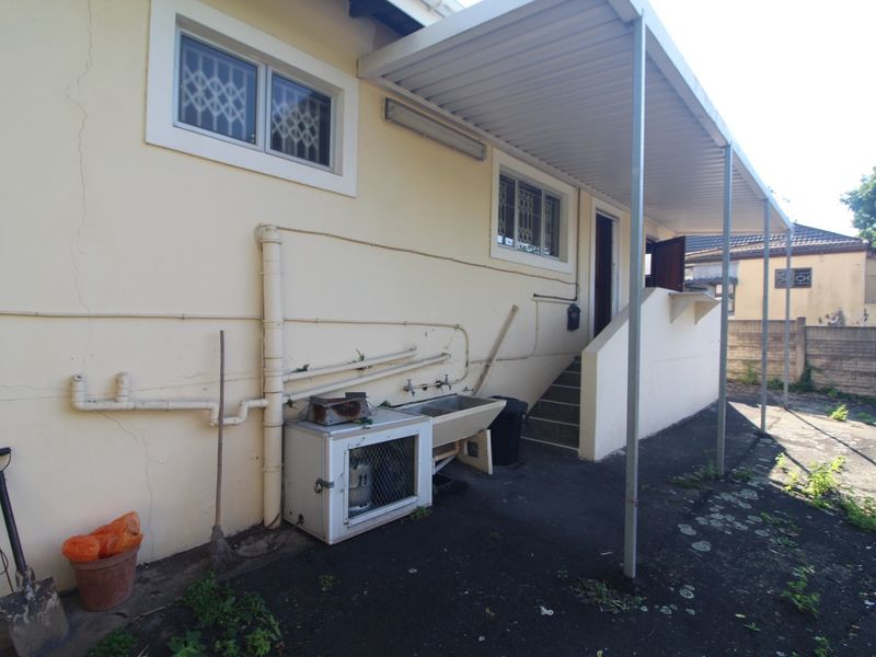 Rear exterior view of the townhouse featuring a covered patio area, utility sink, and external staircase with visible wear to the wall finishes.