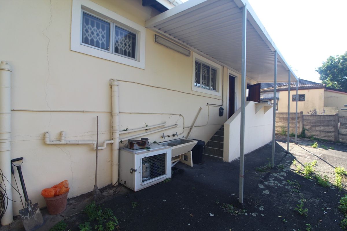 Rear exterior view of the townhouse featuring a covered patio area, utility sink, and external staircase with visible wear to the wall finishes.