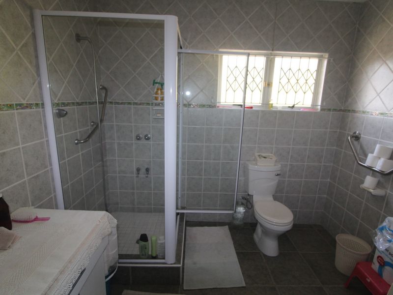 A functional bathroom featuring a shower enclosure, toilet, and safety grab rails, finished with neutral wall and floor tiling.