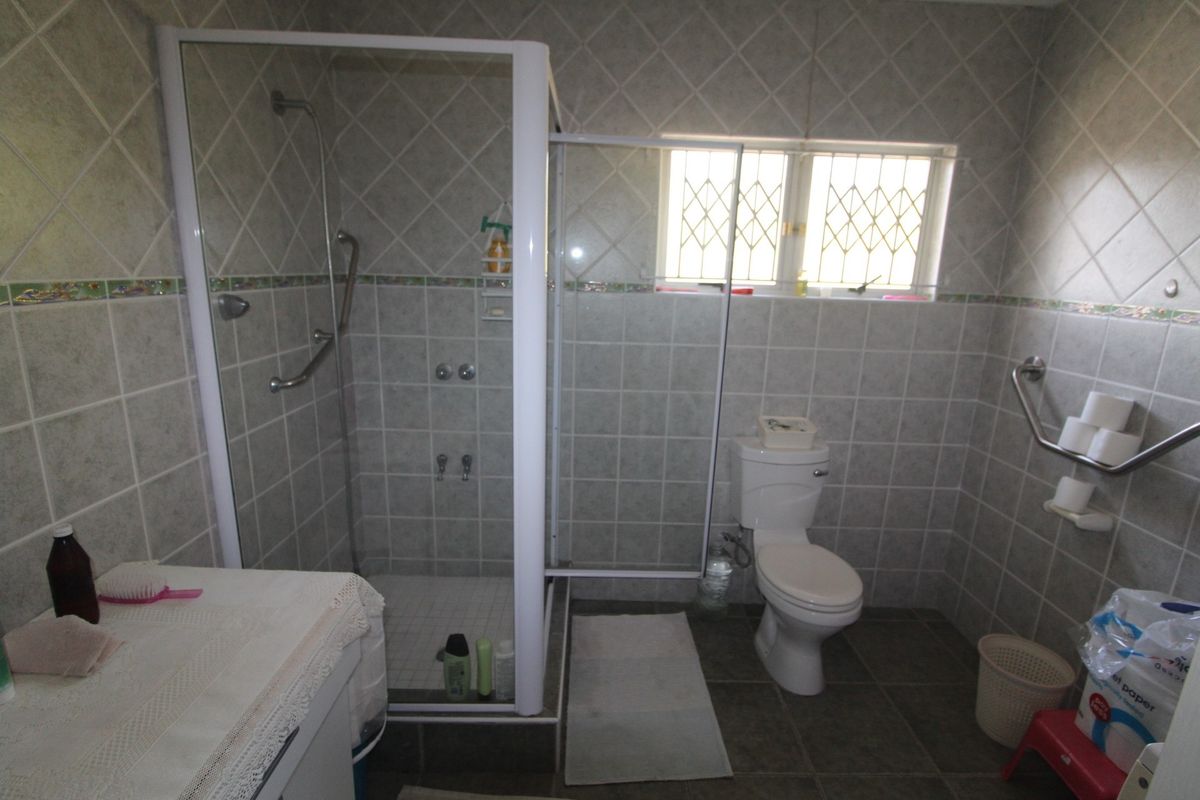 A functional bathroom featuring a shower enclosure, toilet, and safety grab rails, finished with neutral wall and floor tiling.