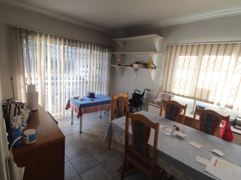 A functional dining area featuring tiled flooring, built-in wall shelving, and large windows with vertical blinds and security gates for added peace of mind.