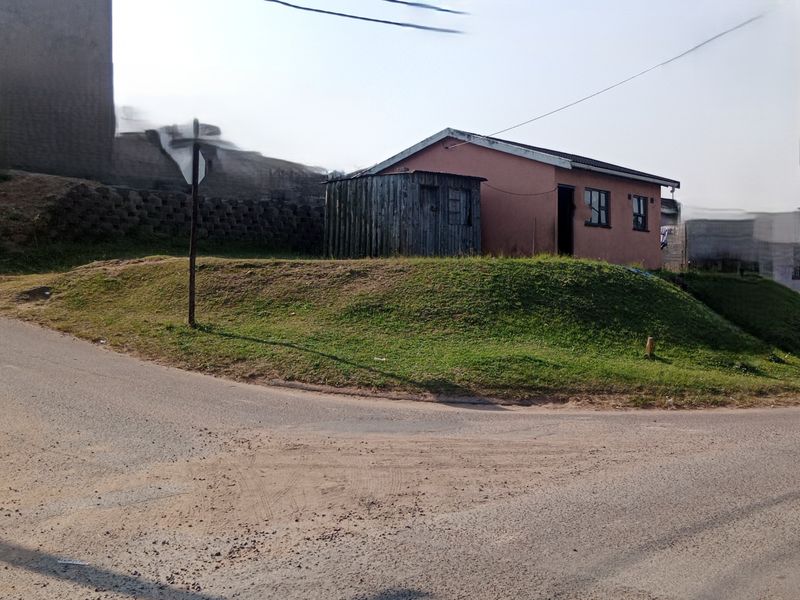 A view of a single-story residential property featuring a small timber shed and a retaining wall, situated on a corner plot.