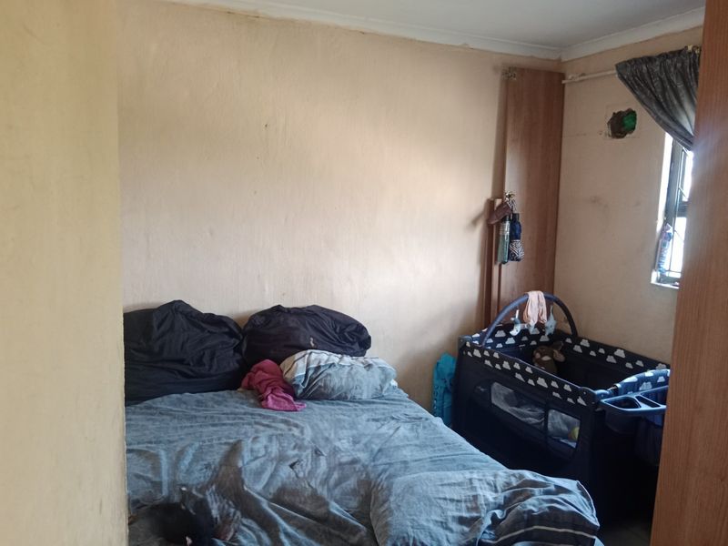 A bedroom featuring a built-in cupboard and window, currently requiring maintenance and cosmetic updates to the wall finishes and electrical fixtures.