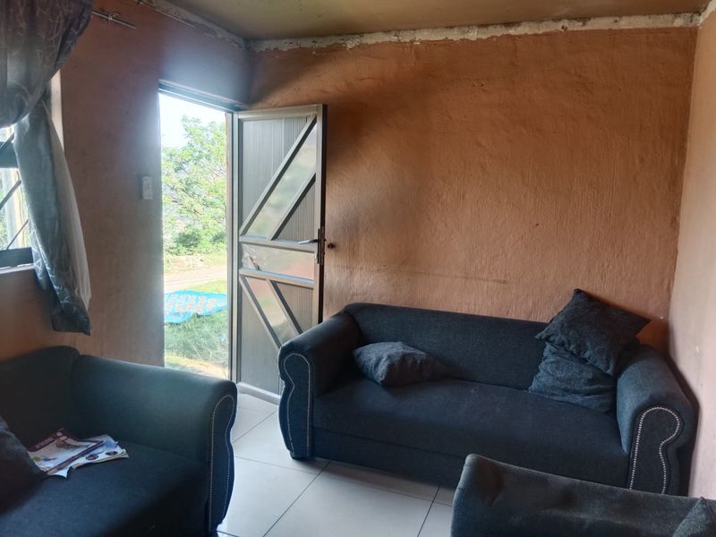A living room area featuring tiled flooring and direct access to the exterior, currently requiring wall finishing and cosmetic updates.