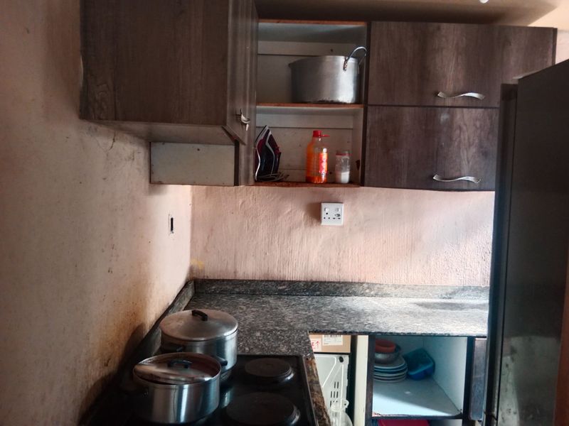 A compact kitchen featuring dark laminate cabinetry, granite countertops, and an integrated electric hob, requiring cosmetic updates to the wall finishes.