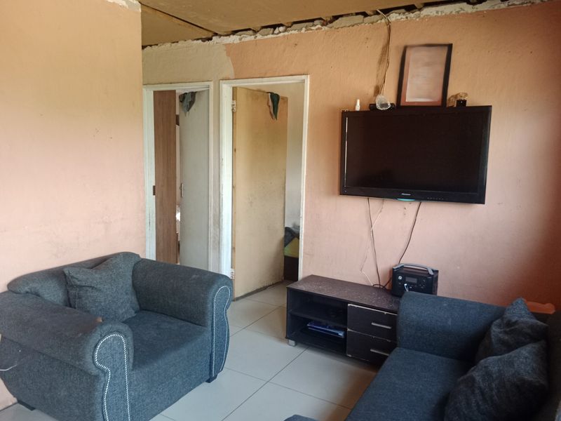 A living room area featuring tiled flooring and internal doors, currently requiring significant cosmetic repairs to the walls and ceiling.