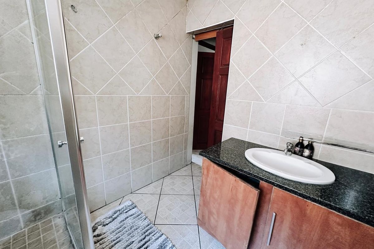 A functional bathroom featuring a shower enclosure, granite-topped vanity with a drop-in basin, and neutral tiled finishes throughout.