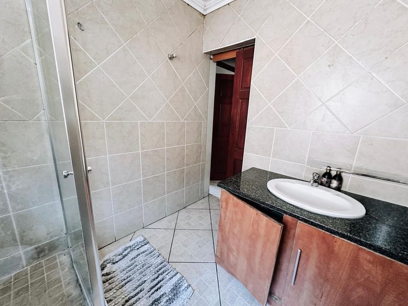 A functional bathroom featuring a shower enclosure, granite-topped vanity with a drop-in basin, and neutral tiled finishes throughout.