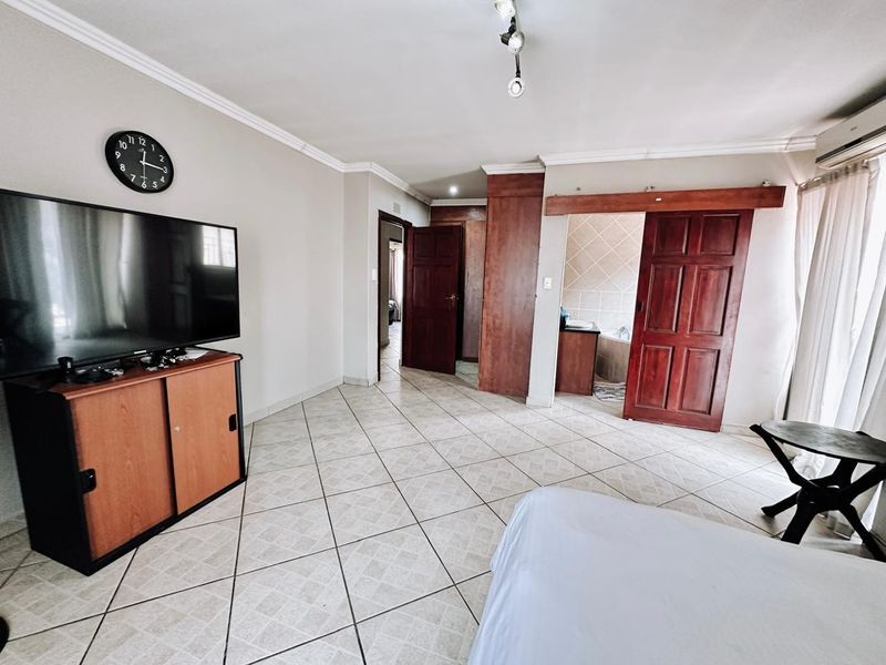 Spacious bedroom featuring tiled flooring, built-in cupboards, and direct access to an en-suite bathroom, complemented by an integrated air conditioning unit.