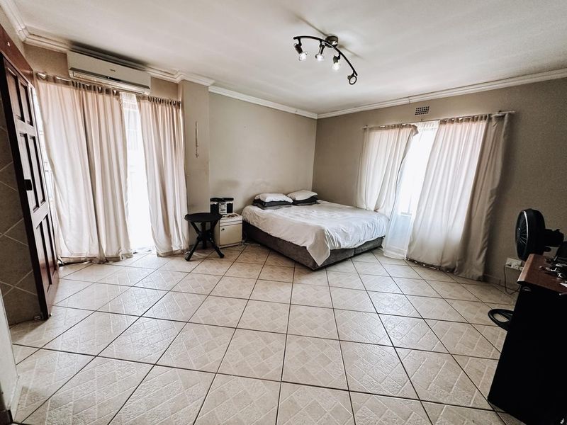 Spacious bedroom featuring tiled flooring, air conditioning, and large windows with curtain rails, offering a neutral canvas for personalization.