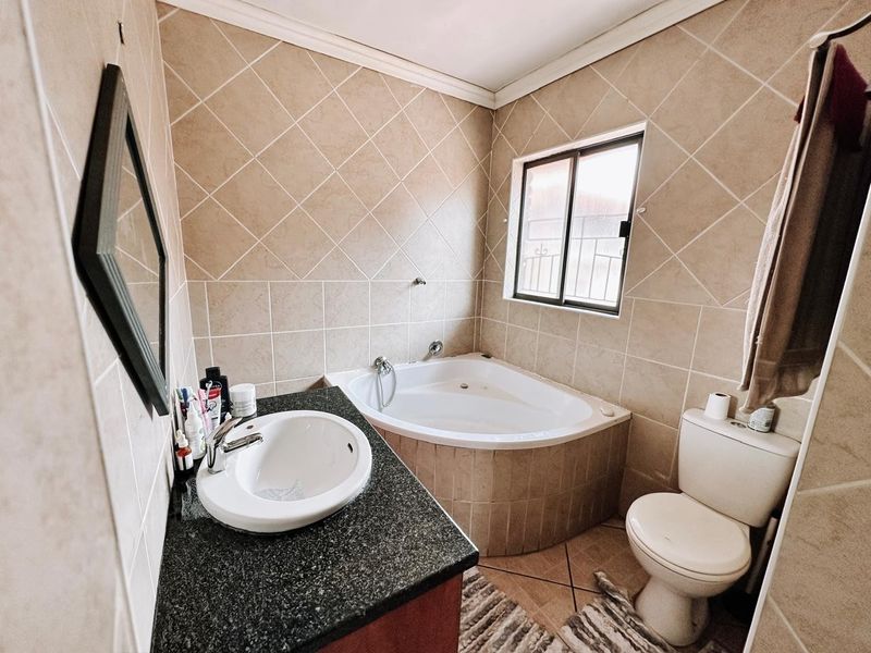 A functional bathroom featuring a corner bathtub, vanity basin with granite countertop, and tiled finishes throughout.