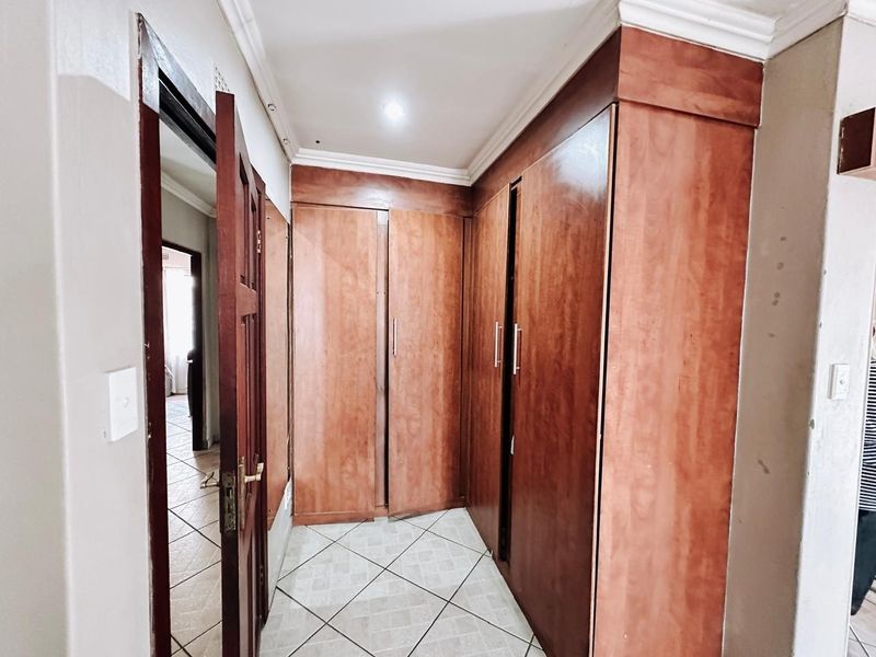 A functional hallway featuring extensive built-in wooden cabinetry, tiled flooring, and classic cornicing, providing ample storage space within the apartment.
