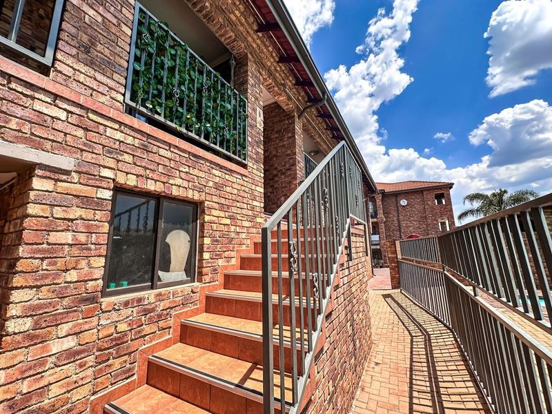 Exterior view of an apartment building featuring a face brick facade, tiled staircase with metal balustrades, and a paved walkway.