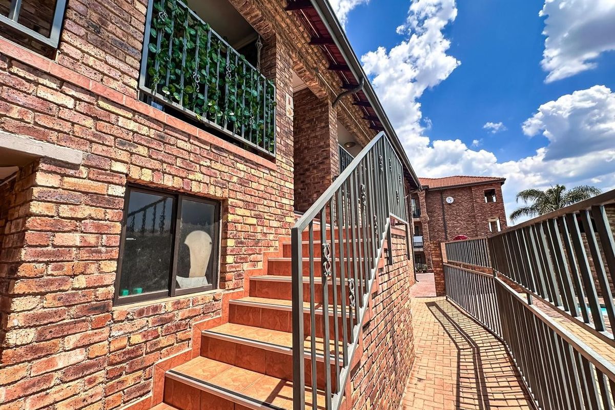 Exterior view of an apartment building featuring a face brick facade, tiled staircase with metal balustrades, and a paved walkway.