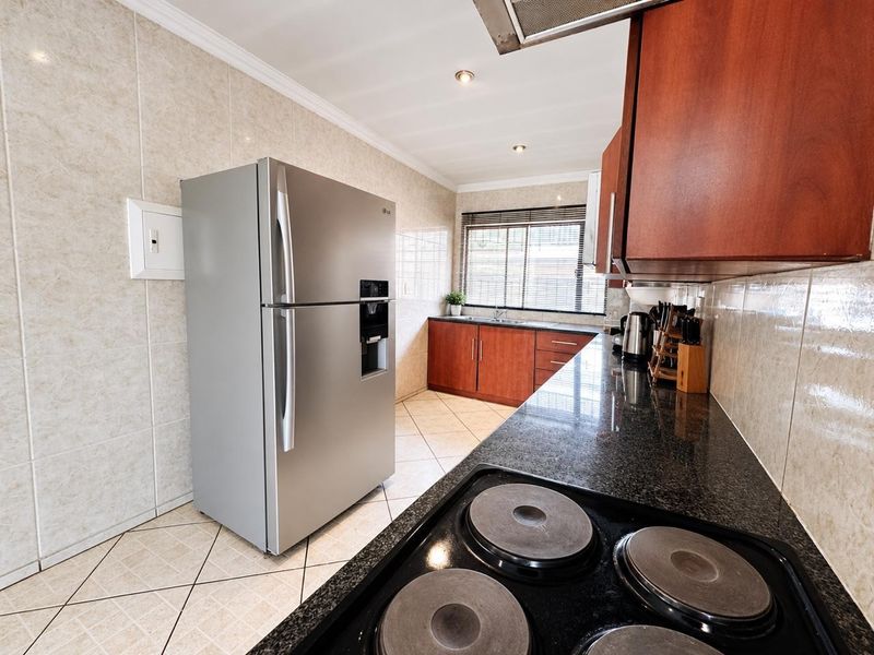 A functional kitchen featuring granite countertops, dark wood cabinetry, tiled walls, and a built-in electric hob with an overhead extractor fan.
